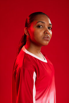 African adult woman posing in studio wearing red athletic jersey with white trim and stud earrings