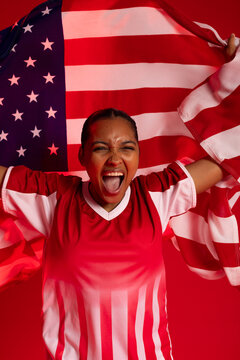 African American woman shouting and holding US flag in studio, wearing red and white jersey