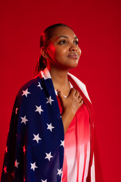 African American woman standing, holding chest, gazing upward red backdrop in US flag red top studs