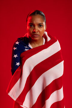 African American woman wrapping self in American flag, posing in studio with red backdrop