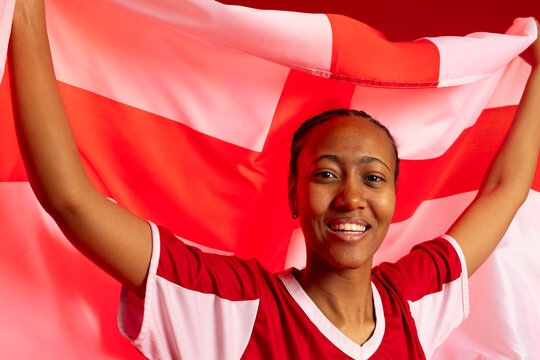 Adult female holding large red-and-white flag behind her, wearing matching sports jersey in studio