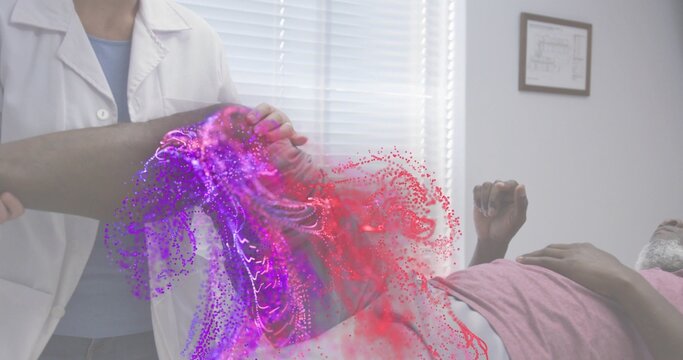Clinician in white-coat holding patient in pink-shirt leg on exam table, purple-red glow on limb