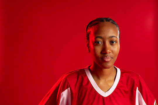 African adult woman wearing red white sport jersey braids stud earring studio backdrop, copy space