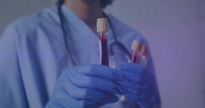 Presenting woman in blue scrubs with stethoscope and blue gloves holding capped blood tubes in lab