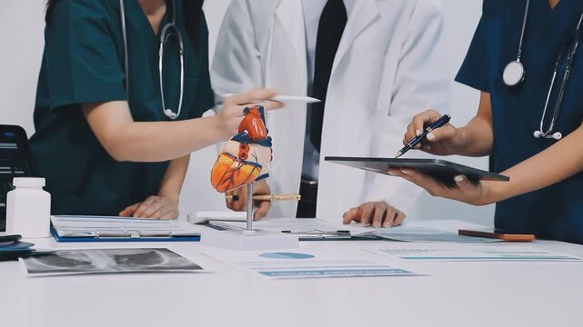 A vibrant red anatomical heart model and a stethoscope on a desk with two doctors having a medical consultation in the background.