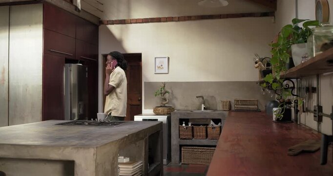 African American man taking call, walking loft kitchen, placing mug on island, processing info