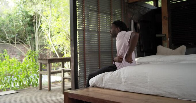 African man sitting on bed rubbing back standing bracing on frame seeking relief, copy space