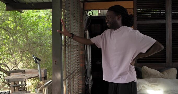 Adult African man pressing lower back in pain, rising bedside, bracing door, gazing out, copy space