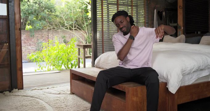 Camera settling, man sitting on wooden bench in bedroom by deck massaging neck relieving tension