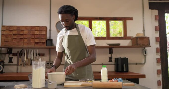 Ring light filming African man in apron cracking eggs adding milk whisking in kitchen for recording