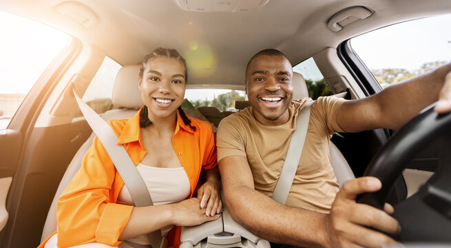 Young African American couple looking at camera inside a car, smiling brightly and posing together, representing happiness, travel lifestyle and positive relationship concept