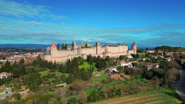 Panoramic view of the medieval city of Carcassonne. Ancient stone walls stretch out beneath a brilliant blue sky, framed by towers with red roofs. France