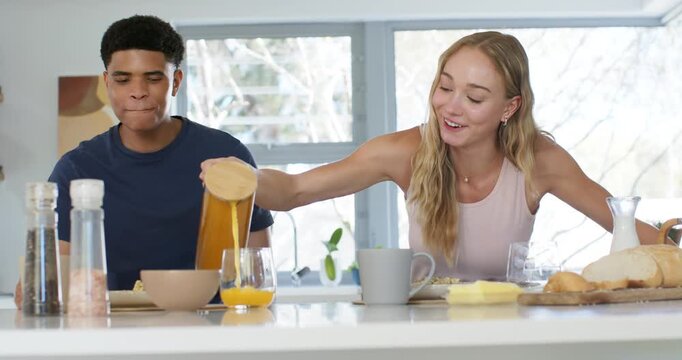 Diverse couple woman reaching across and pouring juice into man's glass during breakfast at home