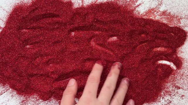A hand erases the inscription 2027 on red glitter. Conceptual, abstract, New Year's or Christmas theme.
