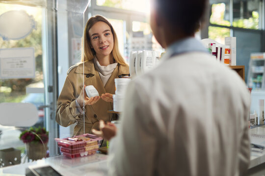 Happy young  woman talking to a pharmacist while buying a medicine in a drug store