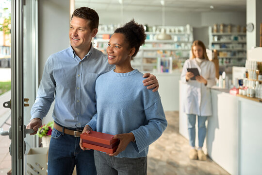 Happy diverse couple going out of drugstore after buying medicines.