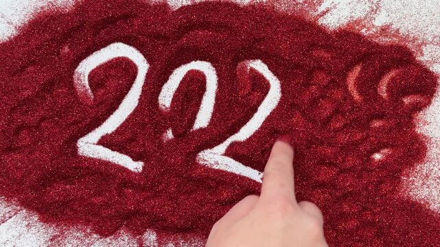 A hand erases the inscription 2027 on red glitter. Conceptual, abstract, New Year's or Christmas theme.