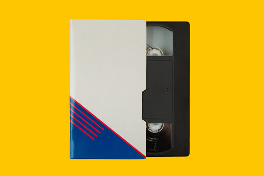 Retro black VHS tape partially inside a white paper sleeve on a yellow back