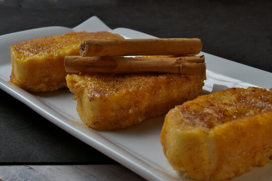 Spanish French toast with cinnamon sticks - Traditional Spanish torrijas with sugar and cinnamon, served on a white plate, perfect for Easter dessert or sweet breakfast.