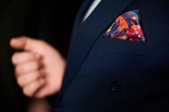 Elegant man adjusting suit with colorful pocket square close up