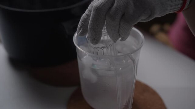 Close-up of person cooling down heated glass bottle in cold water to create diy glassware, showing crafting process of recycling and homemade upcycling of materials in workshop, close-up, slow motion.