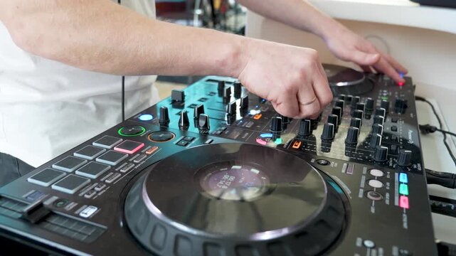 DJ adjusting sound levels on professional mixer with vinyl turntables in a modern studio setting, showcasing precise hand movements