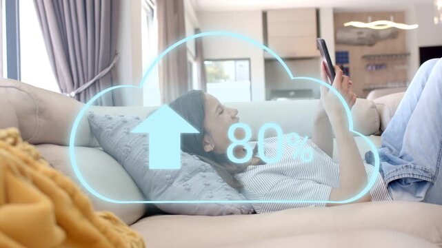 Woman reclining on sofa tapping phone, watching cloud over torso showing upload percent to 100%
