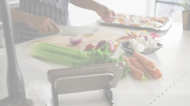 Mid-adult woman slicing onion with chef knife on counter, following tablet recipe and arranging veg