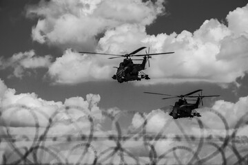 Obraz premium Military helicopters patrolling sky over razor wire fence