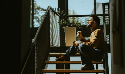 Enjoying a peaceful moment with coffee while sitting on stairs in a cozy space © BGStock72