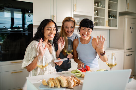 Three friends cooking and waving on video call in modern home kitchen