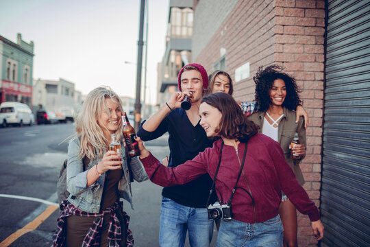 Young friends toasting beers on urban street