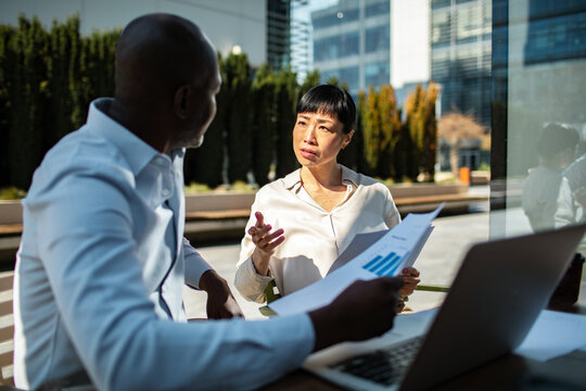Colleagues discussing financial report outdoors at office