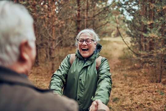 Laughing senior woman holding hands with partner on forest trail