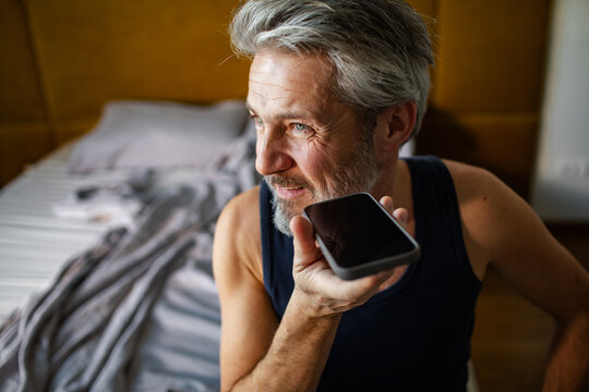 Gray-haired man using smartphone voice assistant at home