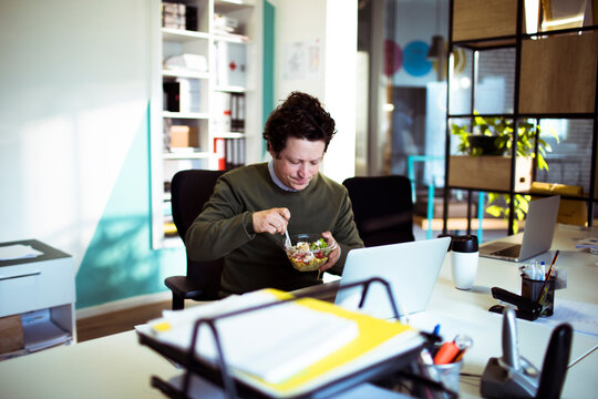 Man eating salad while working at modern office desk