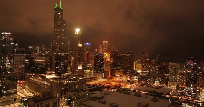 Aerial drone view of Downtown Chicago skyline at night during winter with snowfall and dramatic city lights