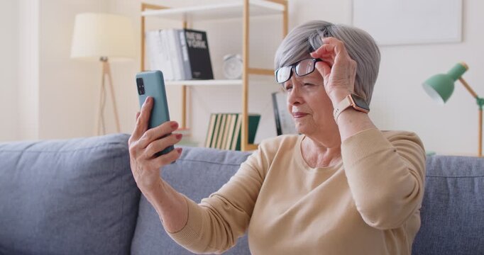 Senior woman with glasses squints, smartphone vision problem. She peers close, adjusting focus eyesight, myopia, hyperopia, presbyopia make reading hard. Key theme age-related vision challenge.