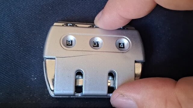 Hand setting the combination code on a silver travel lock, showing a crack, video.