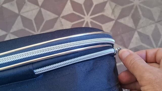 Hand smoothly closing the silver zipper of a black fabric travel suitcase, demonstrating security, video footage.