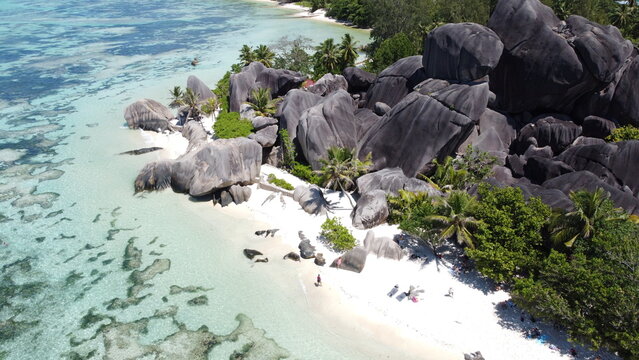 Morges, Switzerland - 11.04.2026: Aerial view of a sandy beach with large granite rocks, turquoise water, and sunbathers near palm trees.