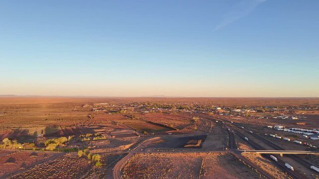 An aerial drone shot capturing a wide expanse of Interstate 40 as it winds past a small desert community in northern Arizona during the golden hour.