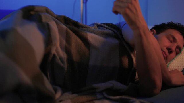 Worker sleeps peacefully. Individual lying awake under blanket. Adult reclines quietly on sofa in dim blue lighting. Peaceful scene of person resting in softly lit living room