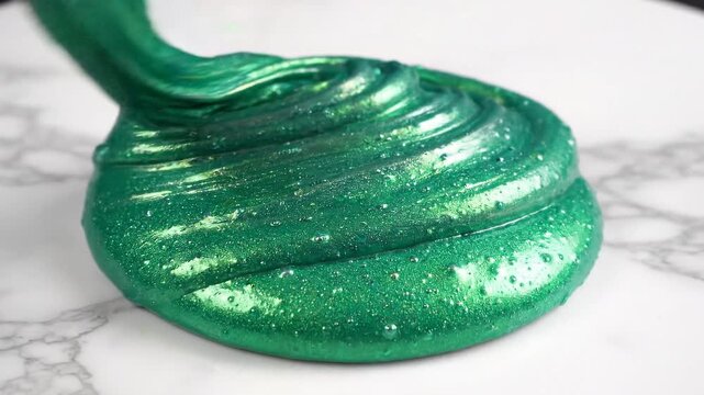 Close-up of vibrant green glitter slime being manipulated on a smooth surface, showcasing its glossy texture and sparkles