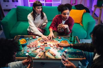 Diverse young friends playing an exciting board game together at home during a fun social gathering © Zamrznuti tonovi
