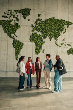 Diverse students talking about global education and environmental sustainability in university hallway with biophilic world map