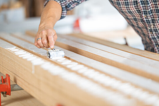 Carpenter applying wood glue with roller on planks