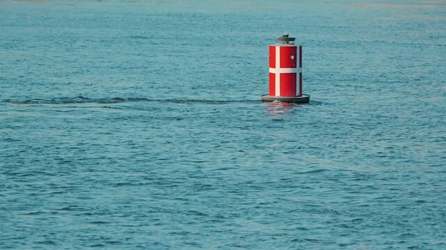 A single red and white navigation buoy floats on the rippling blue surface of a wide river. Minimalist composition with calm, natural lighting. Concept of safety, guidance, and maritime travel