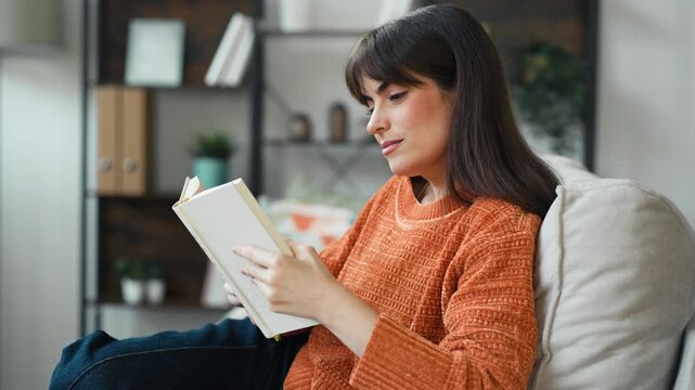 Video of pretty woman reading a book while sitting on the couch at home