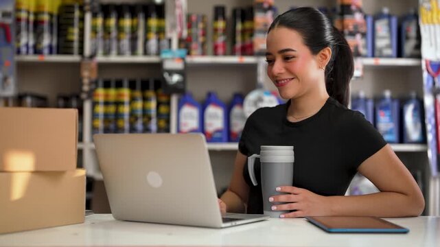 Happy young woman working at her small business, smiling while using her computer in a store